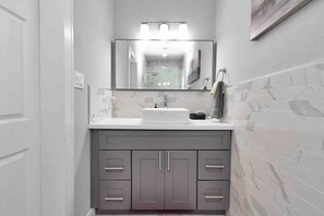 Un baño con lavamanos blanco, un espejo y muebles grises.