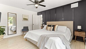 A bedroom with a large bed, a ceiling fan, a bedside table with a lamp, a chair, and a potted plant. - Greenway Getaway Near Silver Springs, walking distance to Cross Florida Greenway (Ocala)
