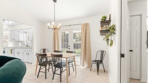 A modern kitchen with white cabinets, a dining area with a wooden table and chairs, and a hanging plant. - Greenway Getaway Near Silver Springs, walking distance to Cross Florida Greenway (Ocala)