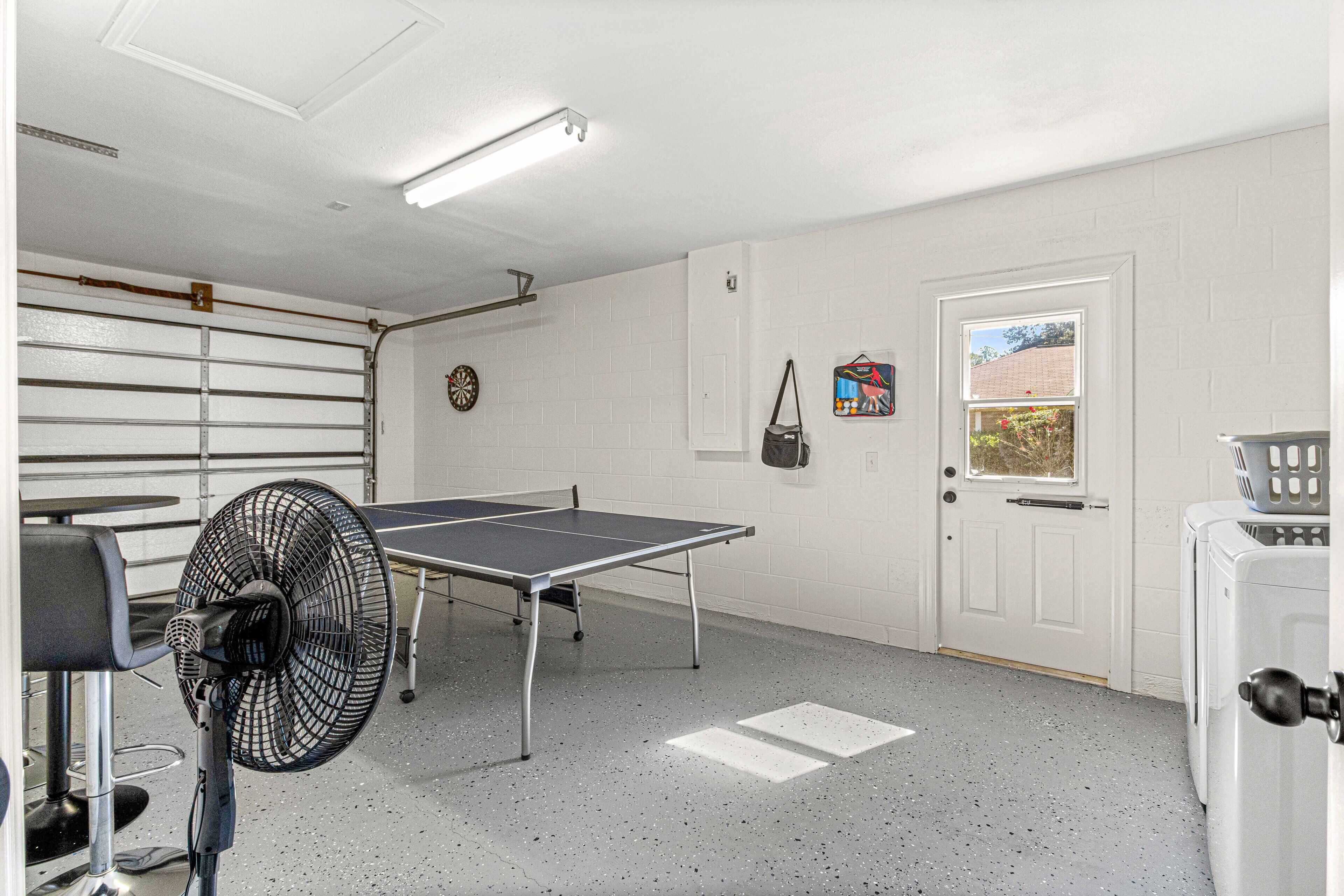 A room with a ping pong table, a fan, a door with a window, and a laundry machine.
