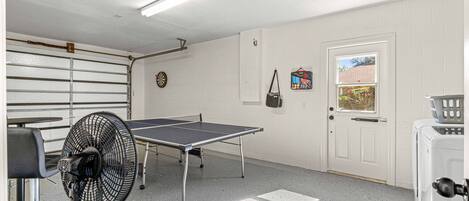 A room with a ping pong table, a fan, a door with a window, and a laundry machine.