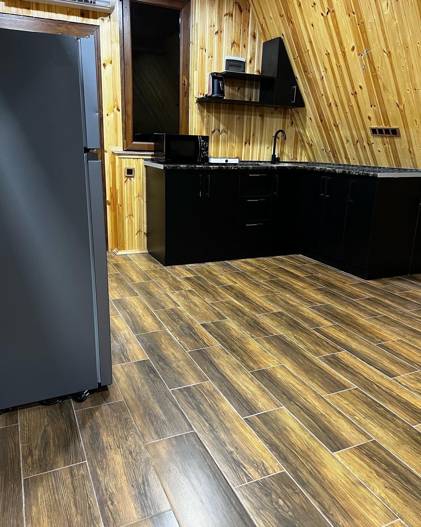 Una cocina con pared de madera, armarios negros y un refrigerador de acero inoxidable.