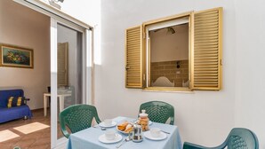 A dining area with a table set for two, a blue tablecloth, and a window with wooden shutters.