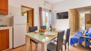 A compact kitchen with a refrigerator, dining table, chairs, and a TV.