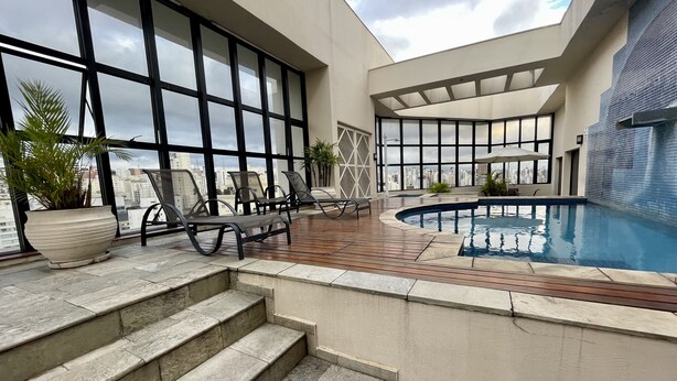 A rooftop pool area with lounge chairs, a small pool, and a view of the city skyline. - Três de Julho Flats - Jardins II (São Paulo)