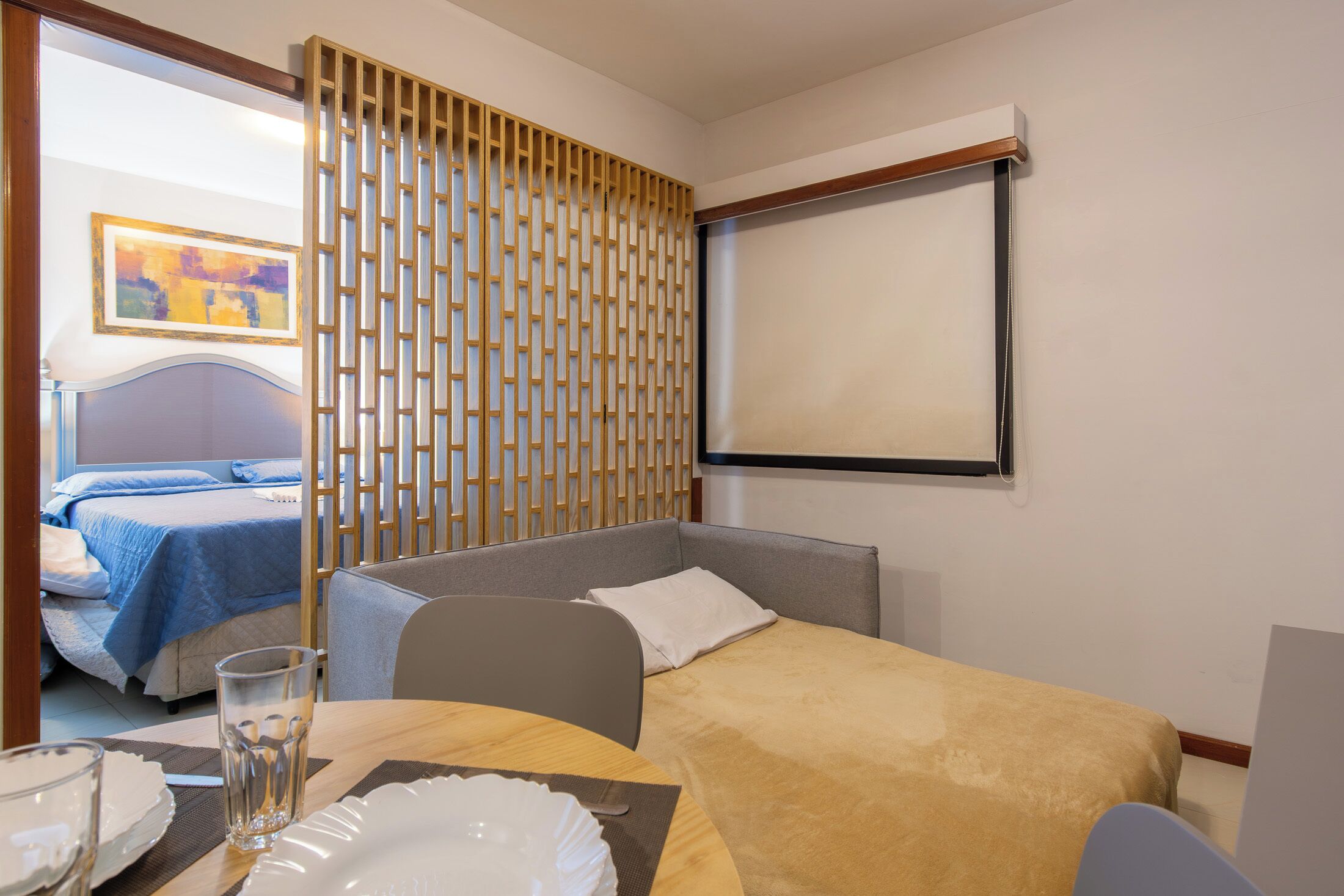 A hotel room with a bed, a desk with a chair, a glass of water, and a television.