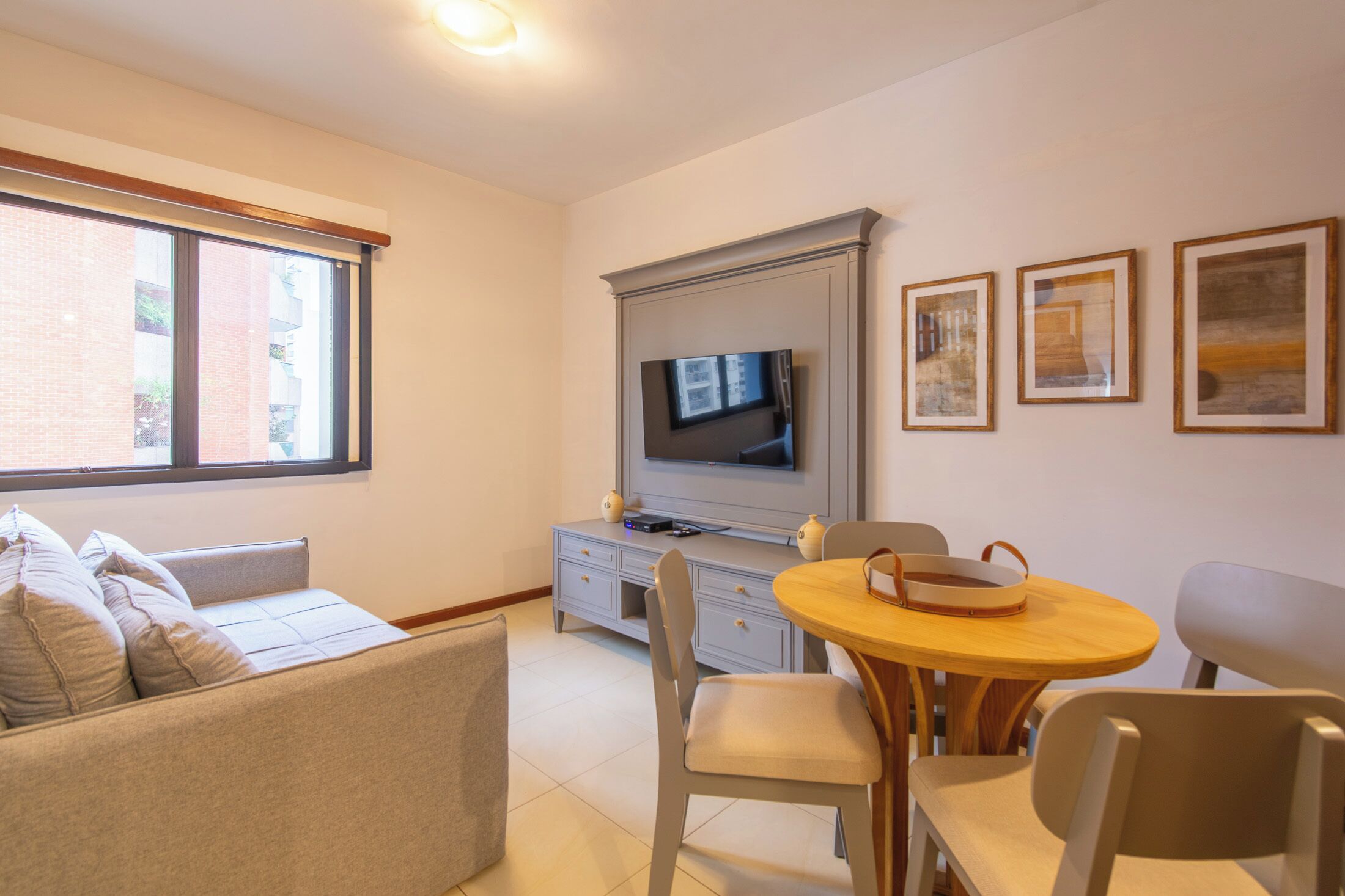 Una sala de estar con un sofá, una mesa de comedor con sillas, un televisor sobre un mueble bajo y cuadros enmarcados en la pared.