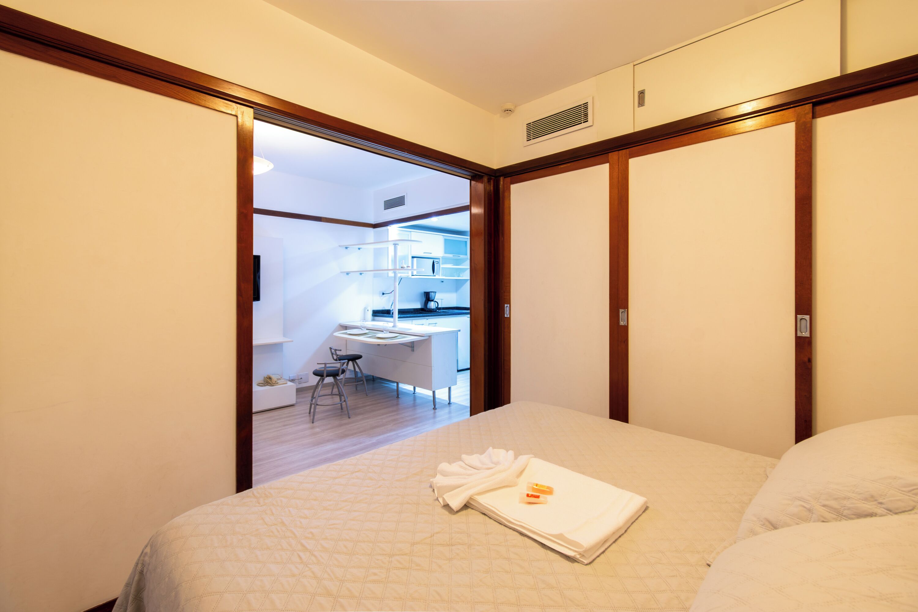 A bedroom with a bed, a desk, and a chair in the adjacent room.