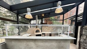 A modern kitchen with a built-in pizza oven, wooden stools, and pendant lighting. - Três de Julho Flats - Jardins II (São Paulo)