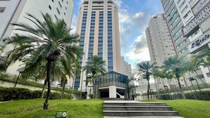 A modern building complex with high-rise residential towers, a central courtyard with palm trees, and a staircase leading to an entrance. - Três de Julho Flats - Jardins II (São Paulo)