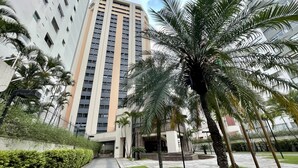 A modern building with a central entrance, surrounded by palm trees and a paved pathway. - Três de Julho Flats - Jardins II (São Paulo)