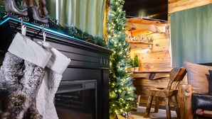 Una habitación acogedora con chimenea, un árbol de Navidad y una pared de madera con un cartel de 'welcome'.