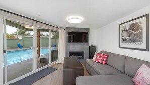 Ett modernt vardagsrum med en grå soffa, en öppen spis och en pool som syns genom glasdörrar.