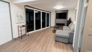 Ett modernt vardagsrum med en grå soffa, en TV som är monterad på väggen och en öppen spis.