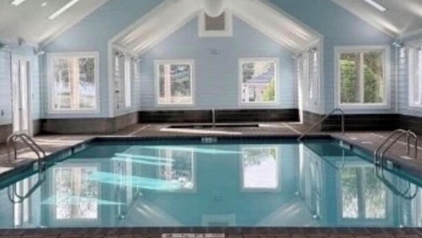 Piscina interior com paredes de vidro transparente, teto em abóbada e várias janelas.