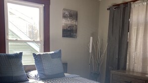 Een slaapkamer met een bed, een raam, een nachtkastje en een wandlamp.