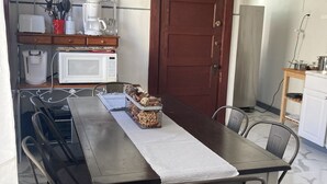 Een eethoek met een tafel, stoelen, een magnetron, een koffiezetapparaat en een kast.