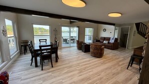 A spacious living room with a wooden floor, a dining area with a table and chairs, a sofa, and a staircase.
