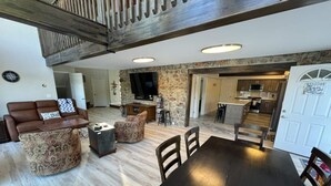 A spacious living area with a dark wooden dining table, patterned sofas, and a stone accent wall.