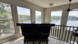 A dining area with a table and chairs, large windows with a view of a lake and trees, and a ceiling fan.