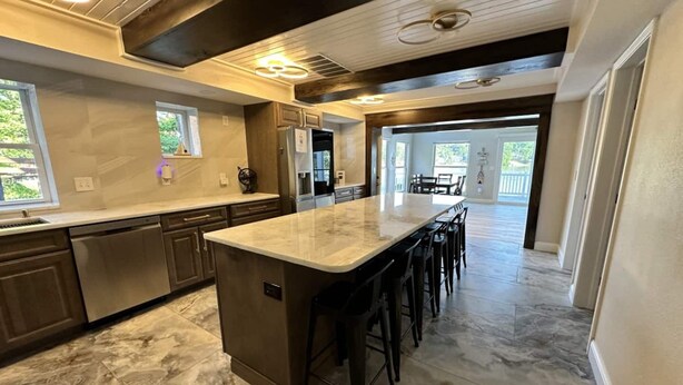 A modern kitchen with a large island, dark wood cabinets, and a marble floor.