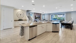 Una cocina moderna con armarios blancos, una isla central con lavavajillas y una zona de comedor con una mesa grande y sillas.