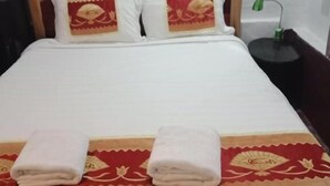 A neatly made bed with a white comforter and two pillows, a red and gold decorative bed runner, and two folded towels on the bed. - Chitlatda Guesthouse (Luang Prabang)