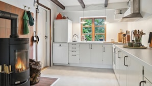 Een moderne keuken met een houtkachel, witte kasten en een raam met uitzicht op groen.