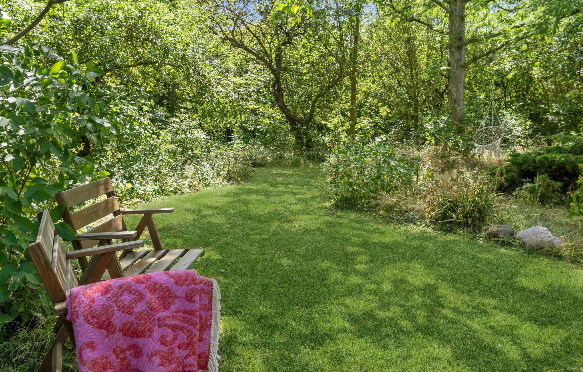 Un banc en bois et une table de pique-nique se trouvent dans un jardin luxuriant, avec un sentier bordé de gazon.