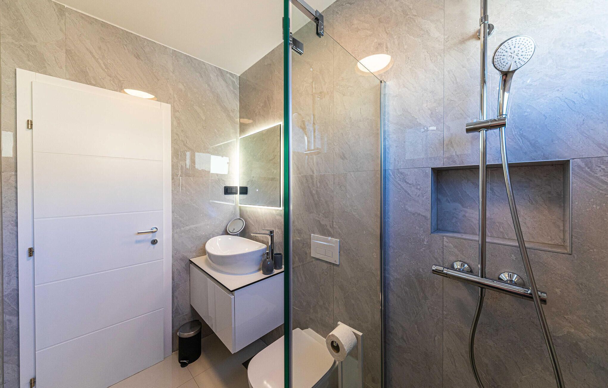 Ein modernes Badezimmer mit einer gläsernen Duschkabine, einem weißen Waschbecken und einer Wand mit Marmorplatten.