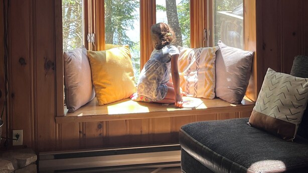 A wooden cabin with a large bay window overlooking a forest.