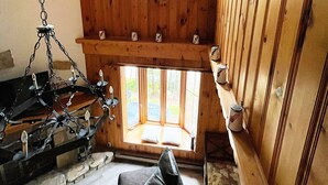 A cozy cabin interior with a stone fireplace, wooden walls, and a window overlooking the outdoors.