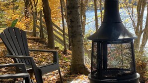 A wooden chair and a black outdoor heater in a forested area with a lake in the background.