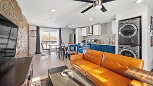 A modern living room with a sofa, a dining area, a kitchen with blue cabinets, and a washing machine.