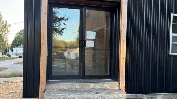 A modern building with a black exterior, a wooden-framed entrance, and a stone staircase leading up to a glass door.