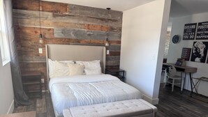 A bedroom with a wooden wall, a bed with a grey upholstered headboard, a bench, and a desk with a chair.