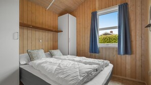 Ett sovrum med en säng, träpanel på väggarna, ett fönster med gardiner och utsikt över grönområden utanför.