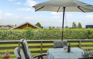 An outdoor patio with a table, chairs, and an umbrella. There is a view of a hedge and a building in the background. - Beautiful home in Sjølund with WiFi (Sjølund)