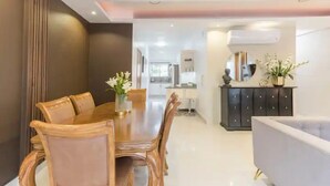 A modern dining area with a wooden table and chairs, a dark cabinet with decorative items, and a light-colored sofa.