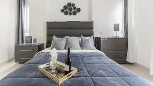 A modern bedroom with a large bed, a bedside table with a bottle, and a decorative wall piece.