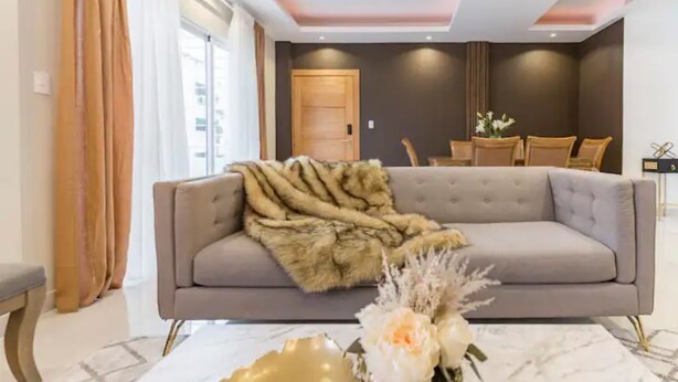 A modern living room with a grey sofa, a fur throw, and a decorative vase on a marble table.