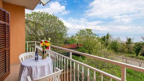 Ein Balkon mit Tisch und Stühlen, einer Blumenvase und Blick auf Grünflächen sowie ein entferntes Gebäude.