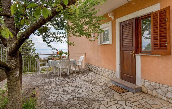 A stone-floored patio with a table and chairs, a wooden door, and a view of the sea.