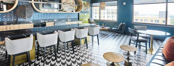 A modern bar area with bar stools, a counter, and a seating area with round tables and chairs.