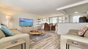 A modern living room with a flat-screen TV, comfortable seating, and a view of the ocean. - Remodeled in 2022, Diamond Head 2 Bedroom Oceanfront condo (Honolulu)