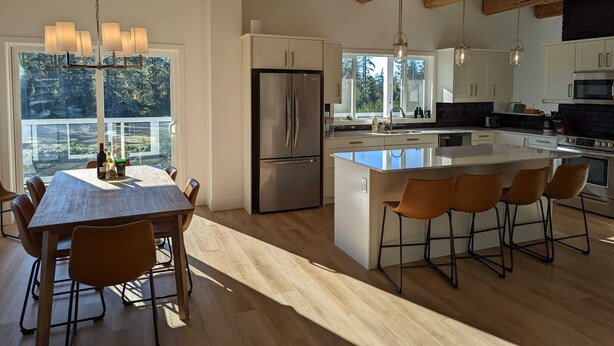 A modern kitchen with a central island, stainless steel appliances, and a large window providing a view of the outdoors. - Beautiful beachfront Villa on 80 acres of farmland! (Sooke)