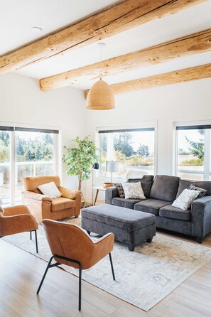 Amplia sala de estar con techo alto, ventanas grandes y una mezcla de muebles, incluyendo un sofá, sillones y una mesa de centro.