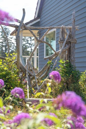 Una estructura de madera con cuerdas, rodeada de follaje y flores moradas.