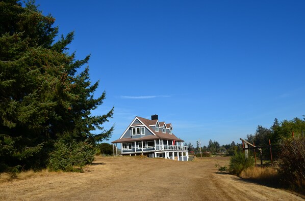A large two-story house with a prominent porch and a large front yard. - Beautiful beachfront Villa on 80 acres of farmland! (Sooke)