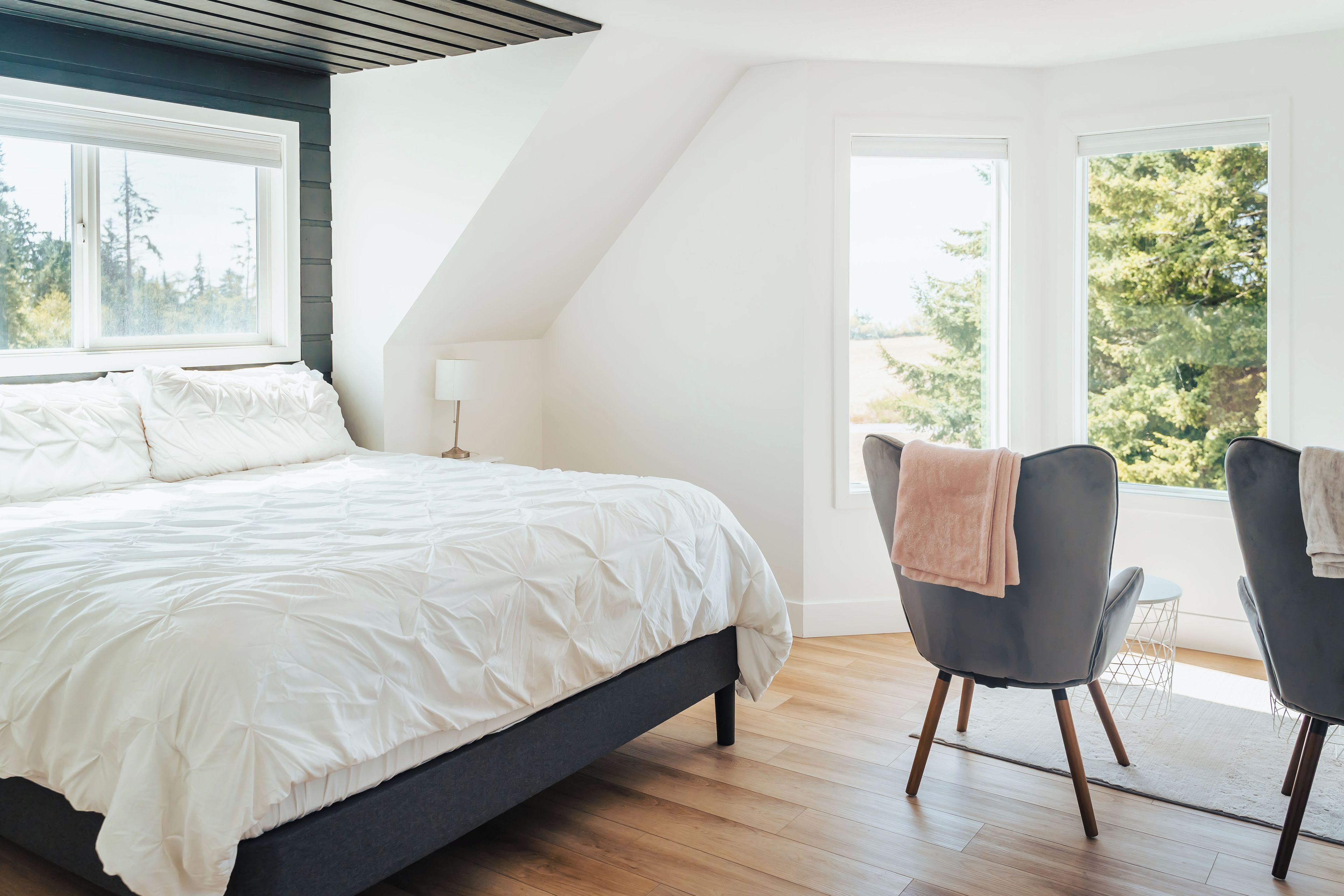 A bedroom with a large bed, a chair, and a view of trees through the window.